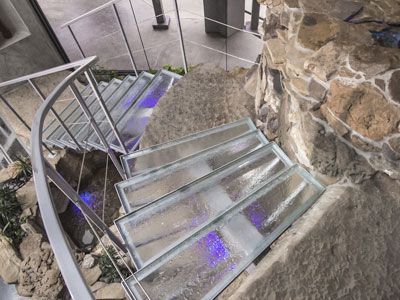 A spiral staircase with glass steps and a stone wall in the background.