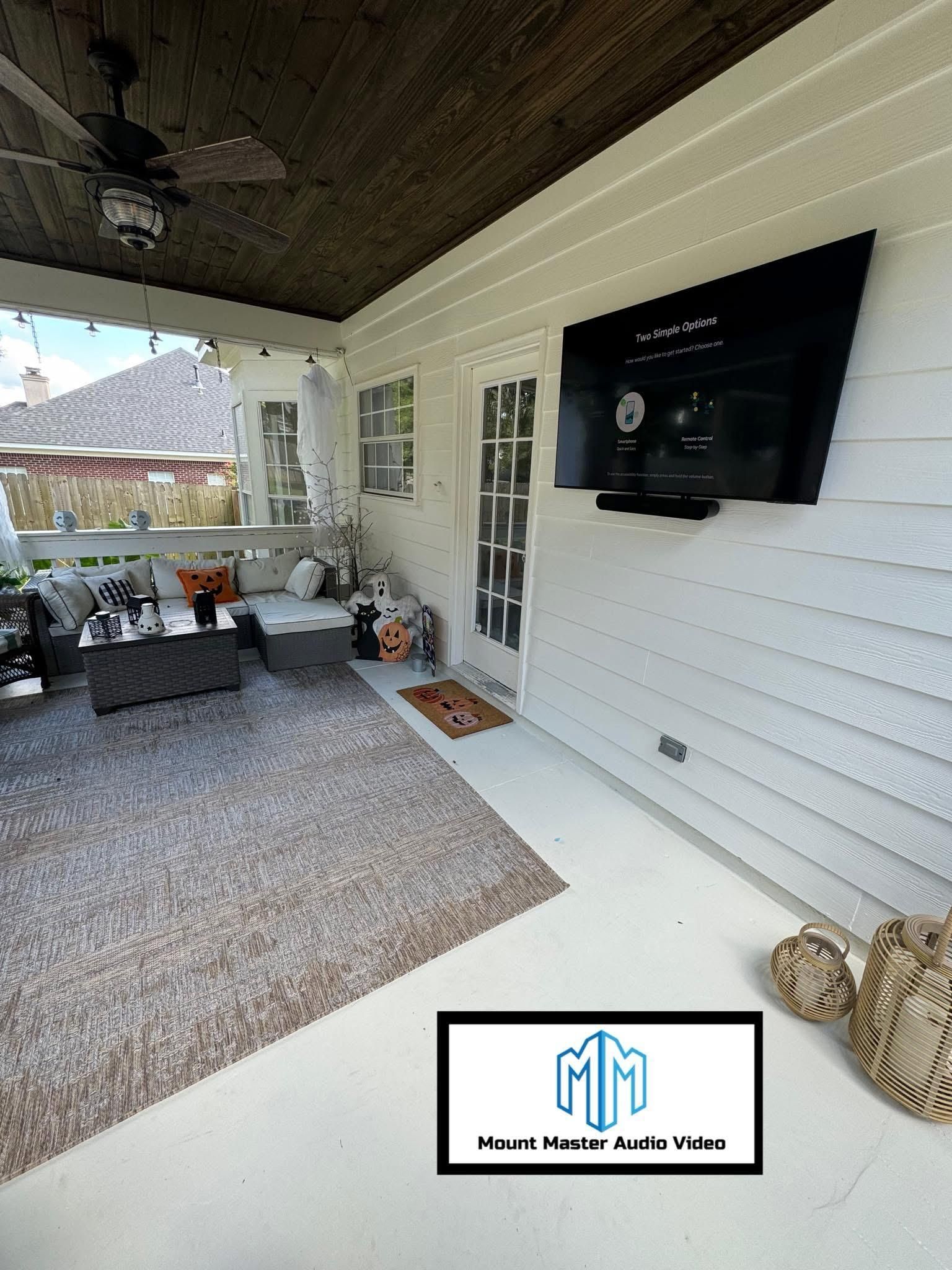 Outdoor patio with a TV, rug, seating, and decorative items.