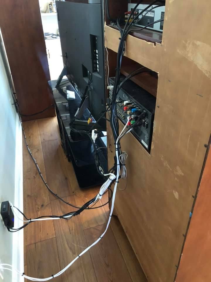 A TV and entertainment system with messy cables in a wooden cabinet, against a wood floor.