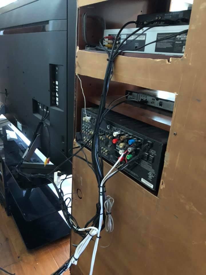 Back of a TV entertainment center with tangled black and white wires; DVD player, receiver, and TV visible.