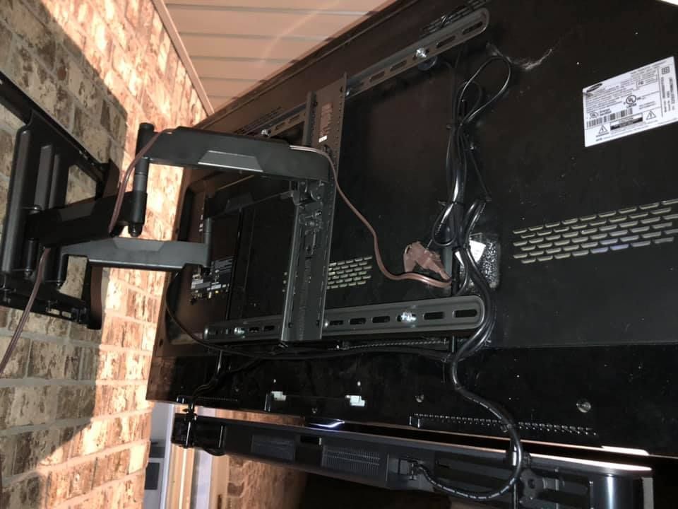 TV mounted on a brick wall with a black articulating arm, revealing the back of the TV and cabling.