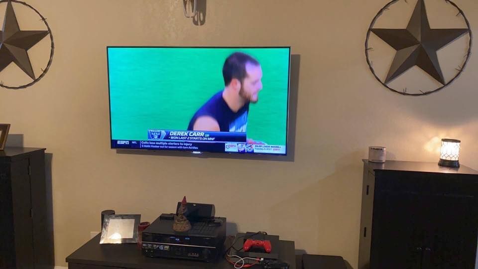 Living room with a TV showing a man on a green screen, flanked by speakers and star decorations.
