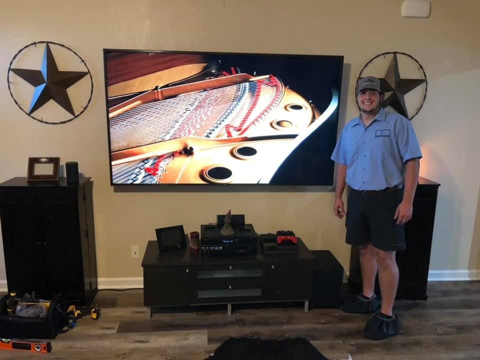 Man stands in front of a large TV. Two star decorations flank the screen. Speakers on either side.