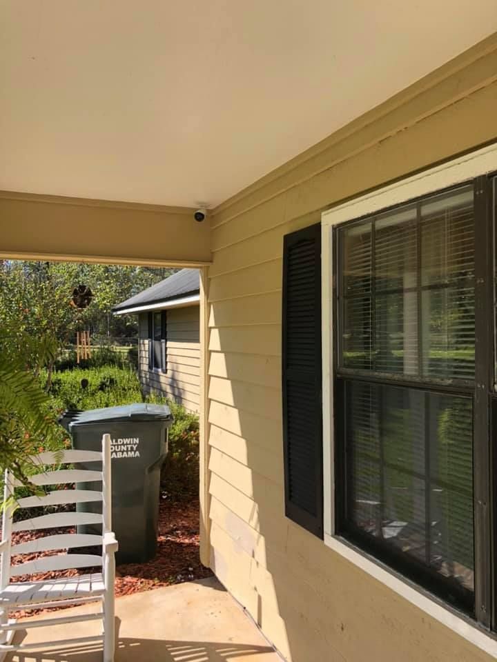 Exterior view of a house with a window, black shutters, and a porch with a rocking chair and a garbage can.