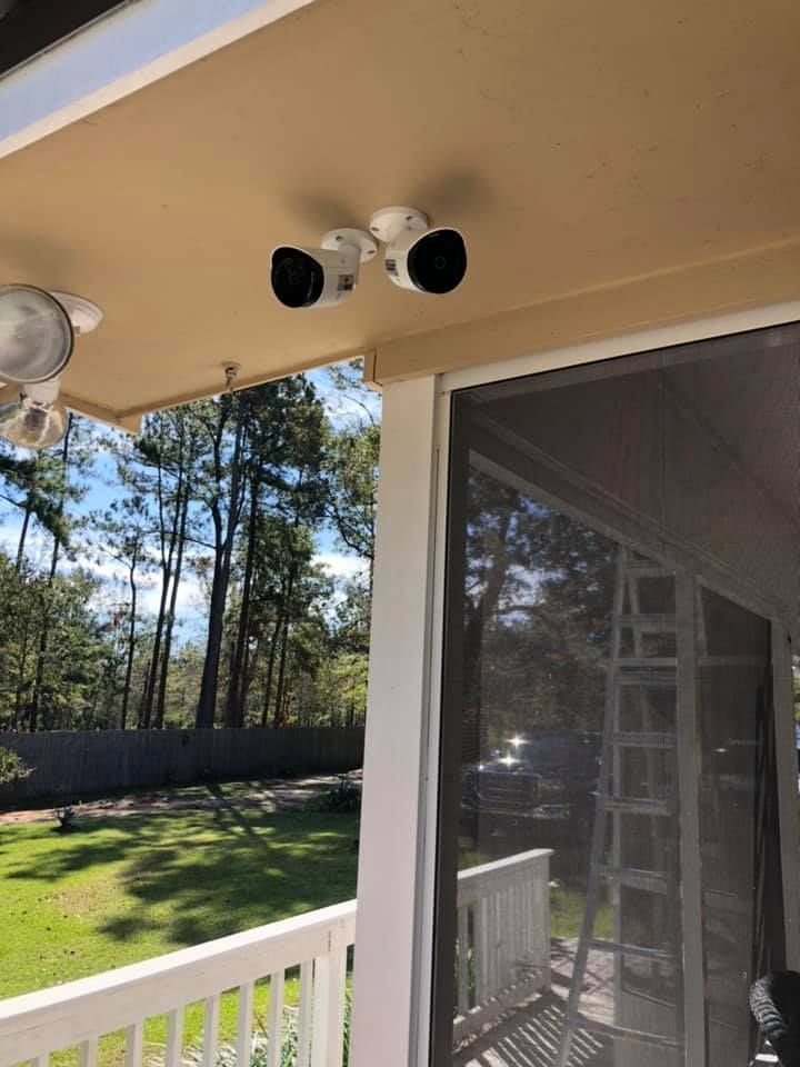 Security lights mounted on a porch ceiling, overlooking a backyard with trees and a screen.