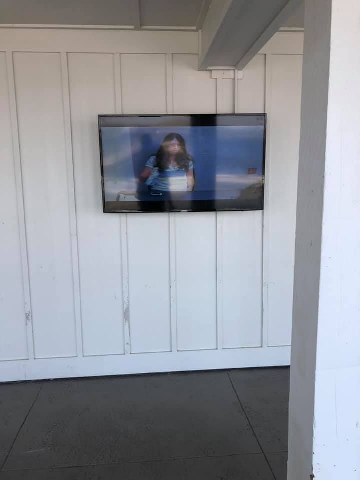 TV screen on a white wall showing a woman standing outside.