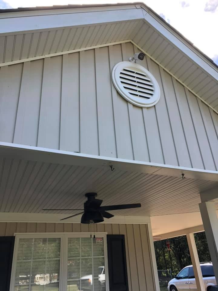 Exterior of a house with vertical siding, an air vent, and a porch with a ceiling fan.