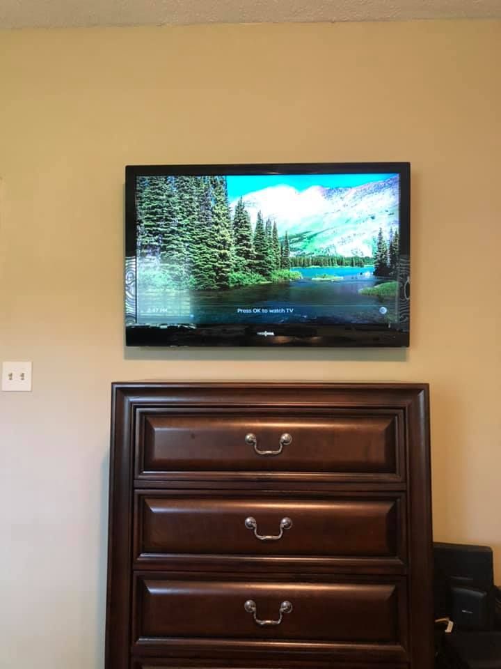 TV displaying a lake scene mounted on a beige wall above a dark wood dresser.