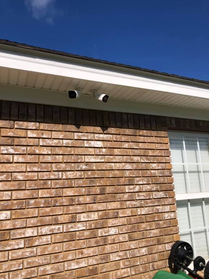 Two security cameras mounted on a brick building's exterior, below a white eave, against a blue sky.