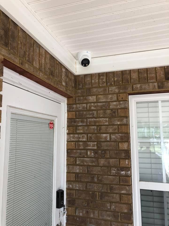 Security camera mounted on a brick wall above a white door and window.