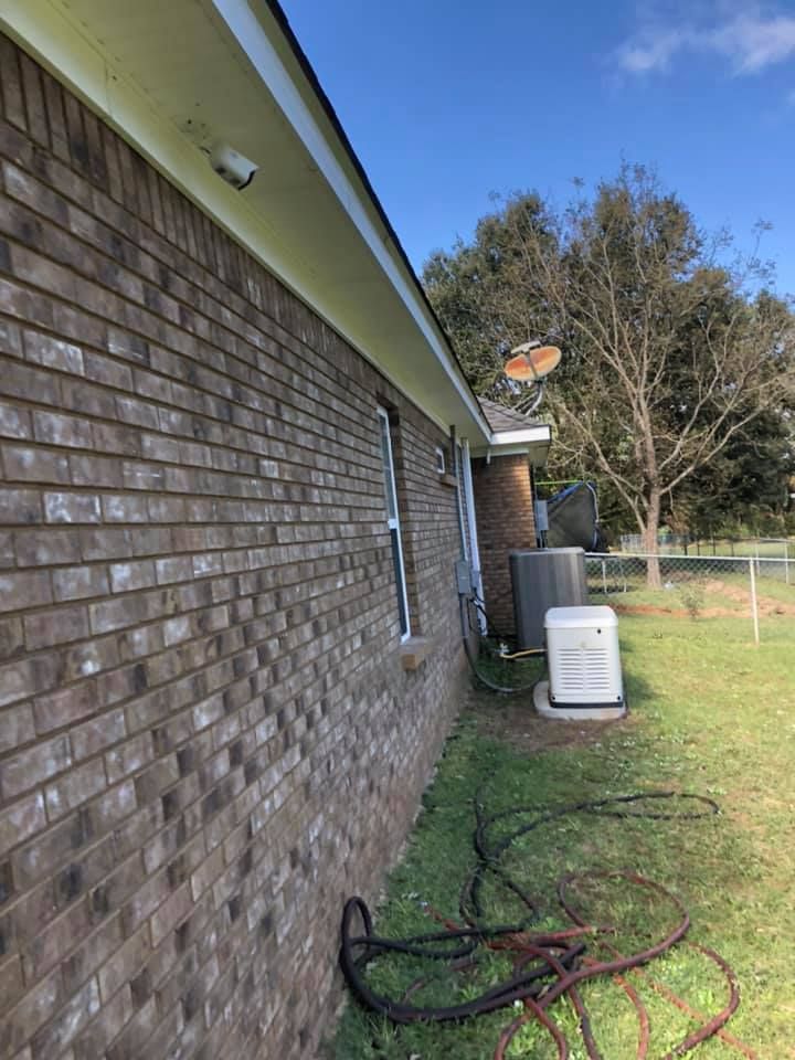 Brick house exterior with security camera, satellite dish, AC unit, and generator on a grassy lawn.