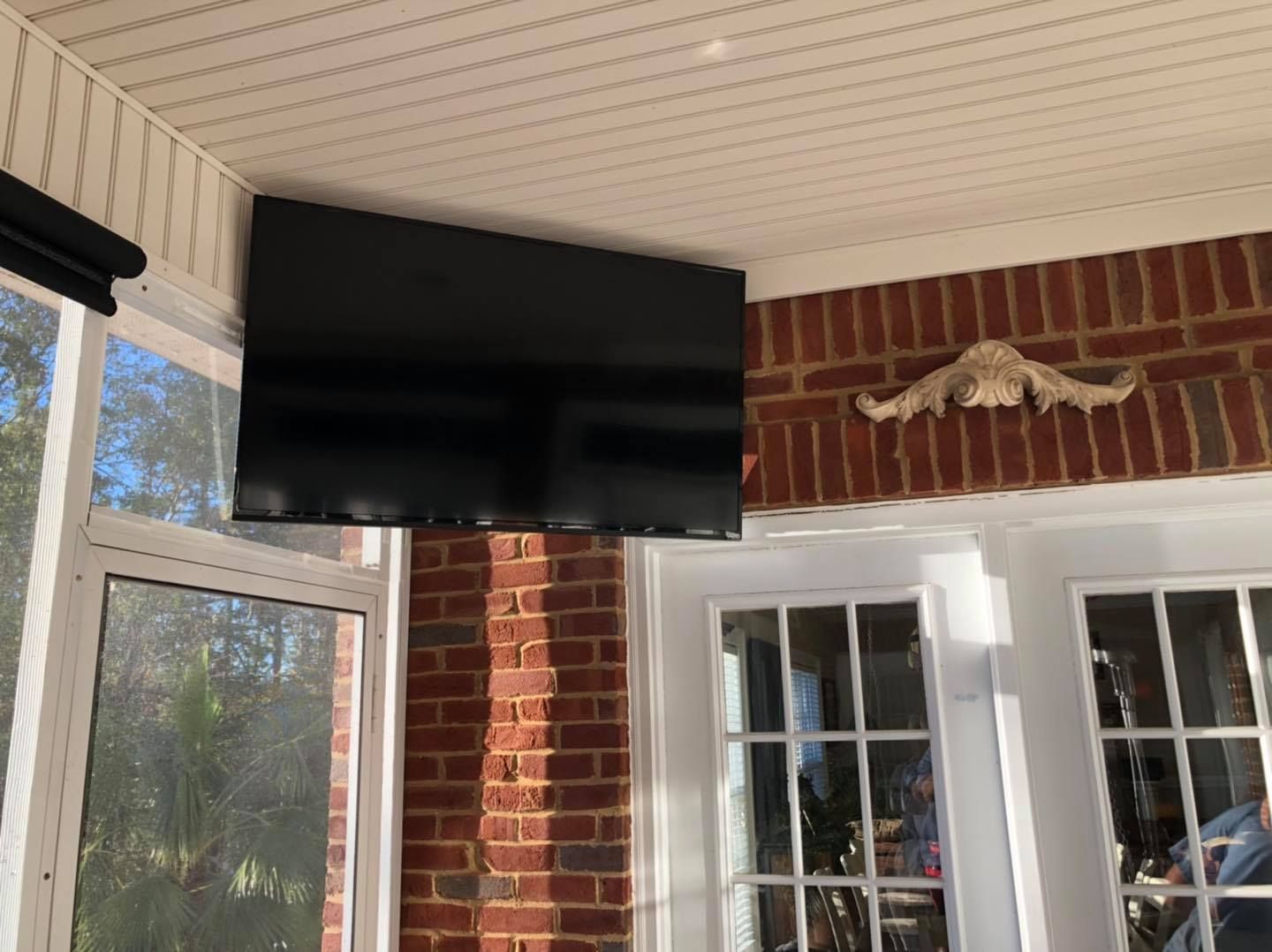 TV mounted on a brick wall in an outdoor space with glass doors and windows.