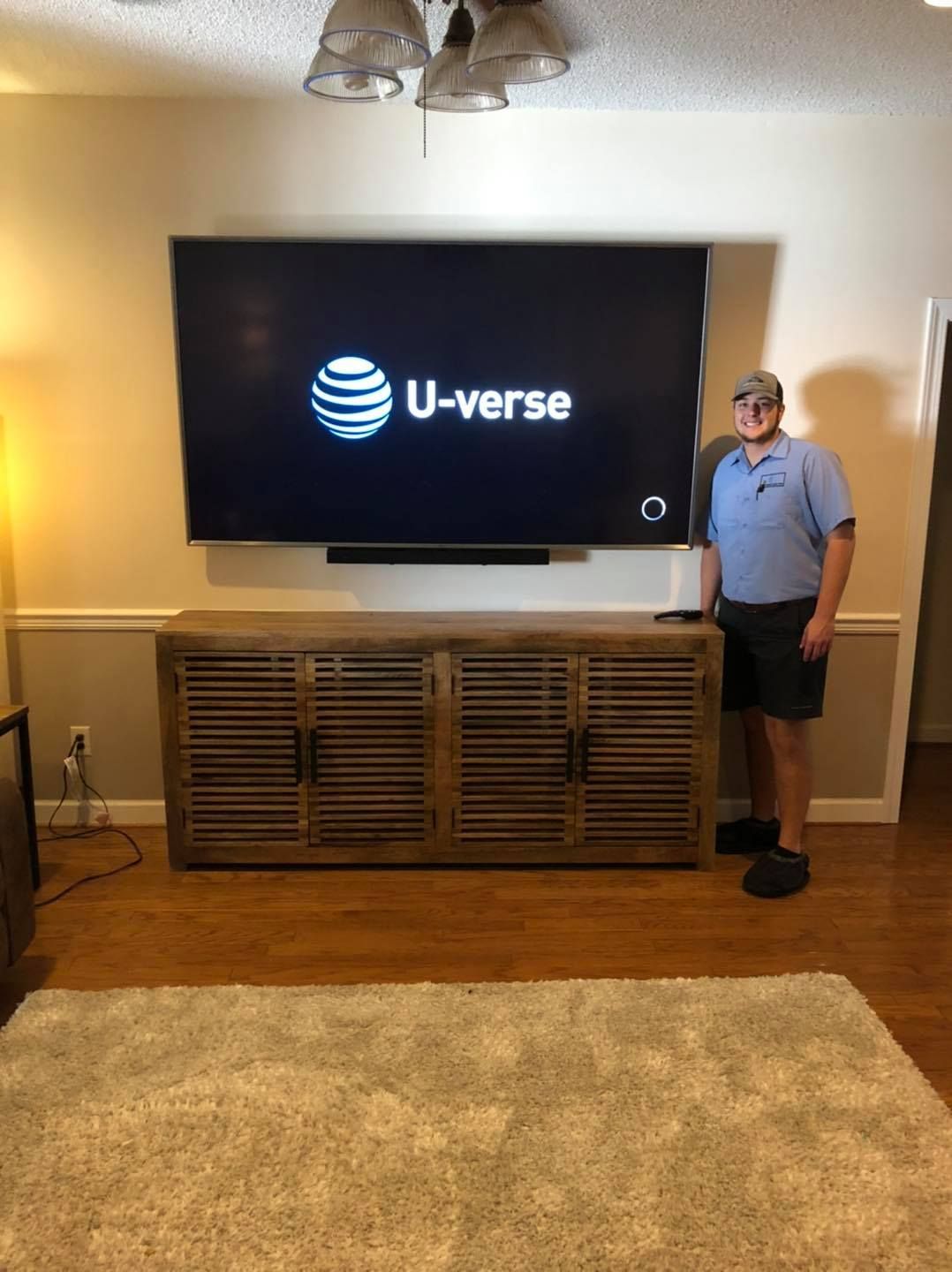 Man stands near large TV, cabinet, and rug in a living room. The TV displays the AT&T U-verse logo.