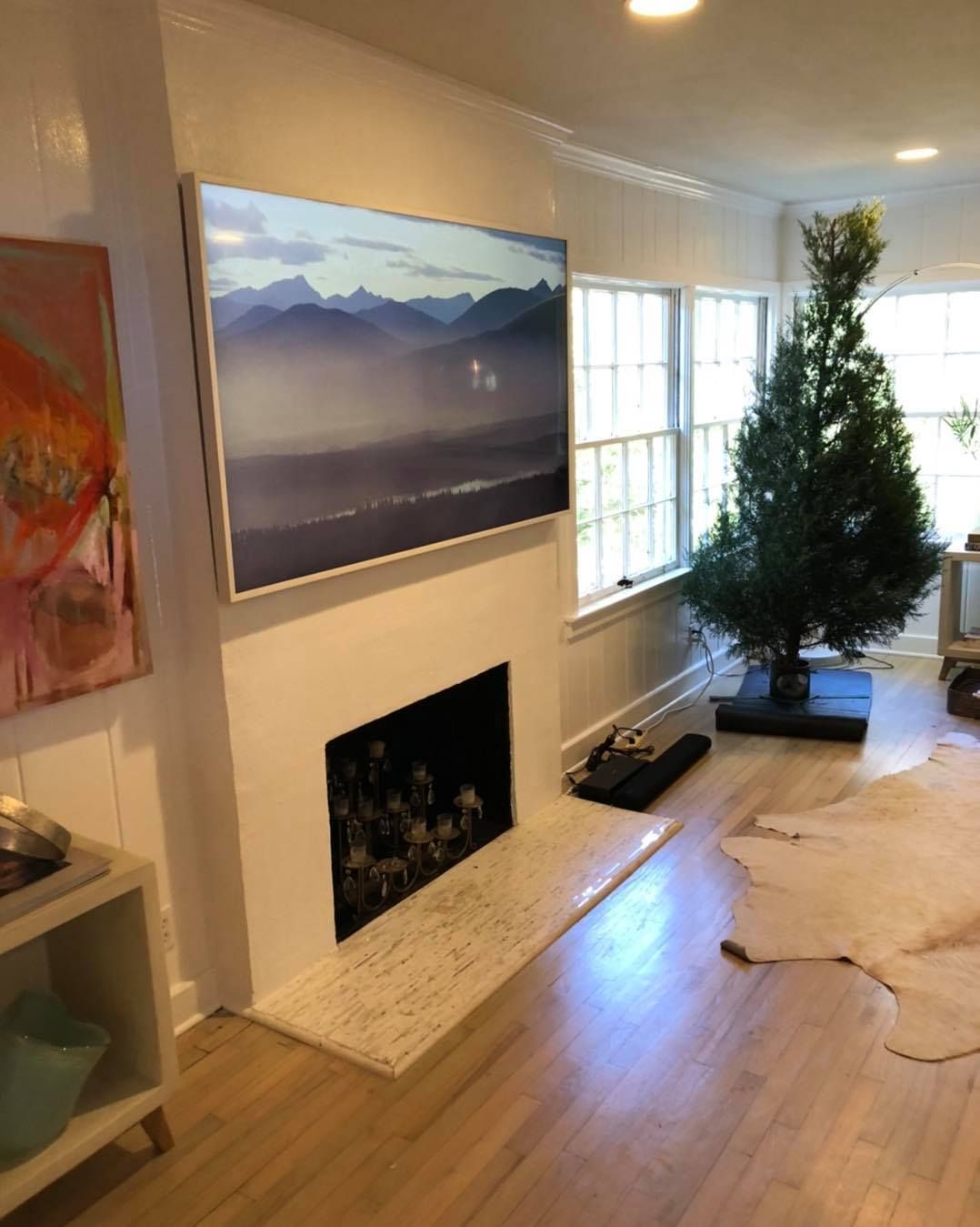 Living room with a mounted TV above a fireplace, a Christmas tree, and a cowhide rug on wooden floors.