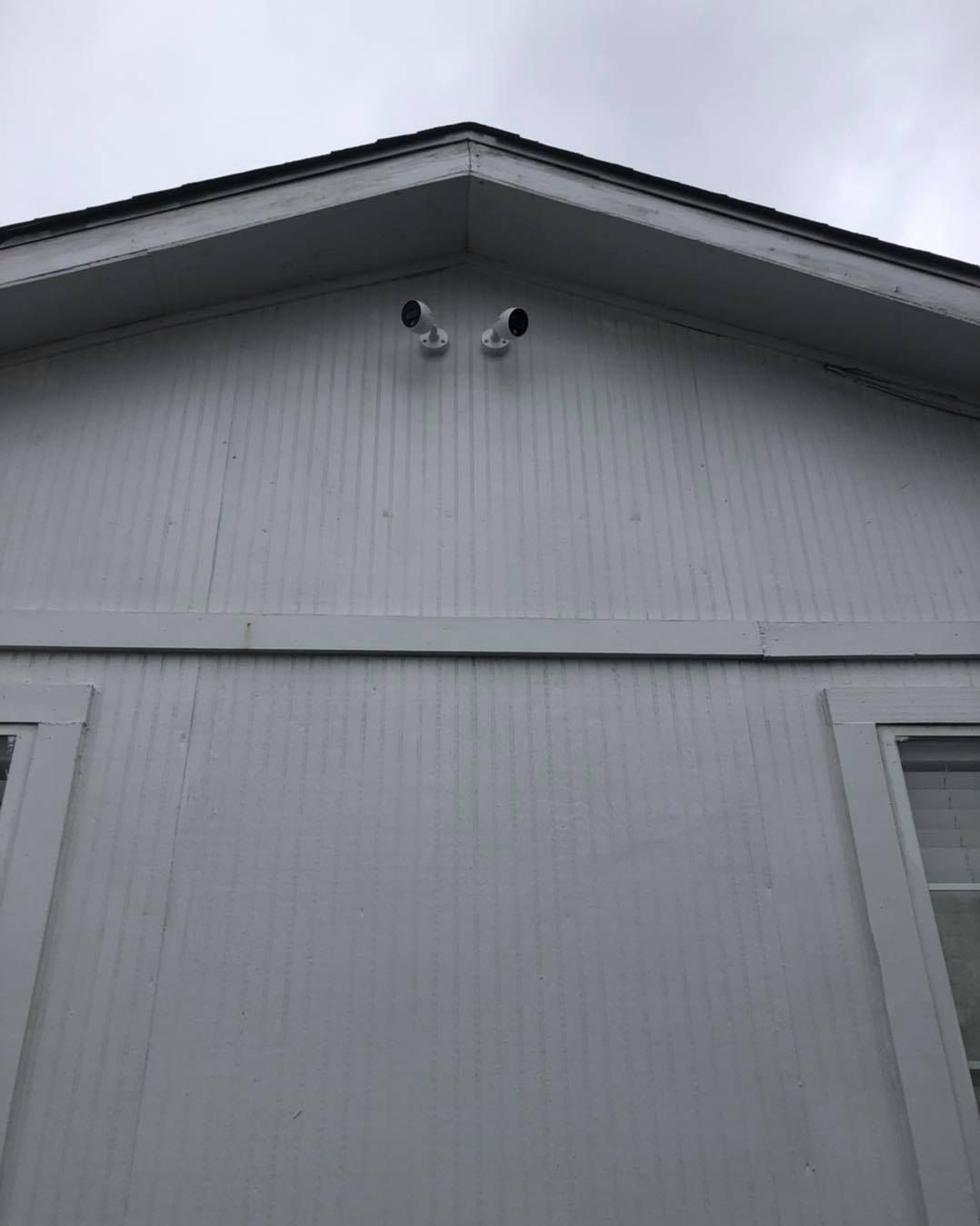 Two security cameras mounted on a white building under a cloudy sky.