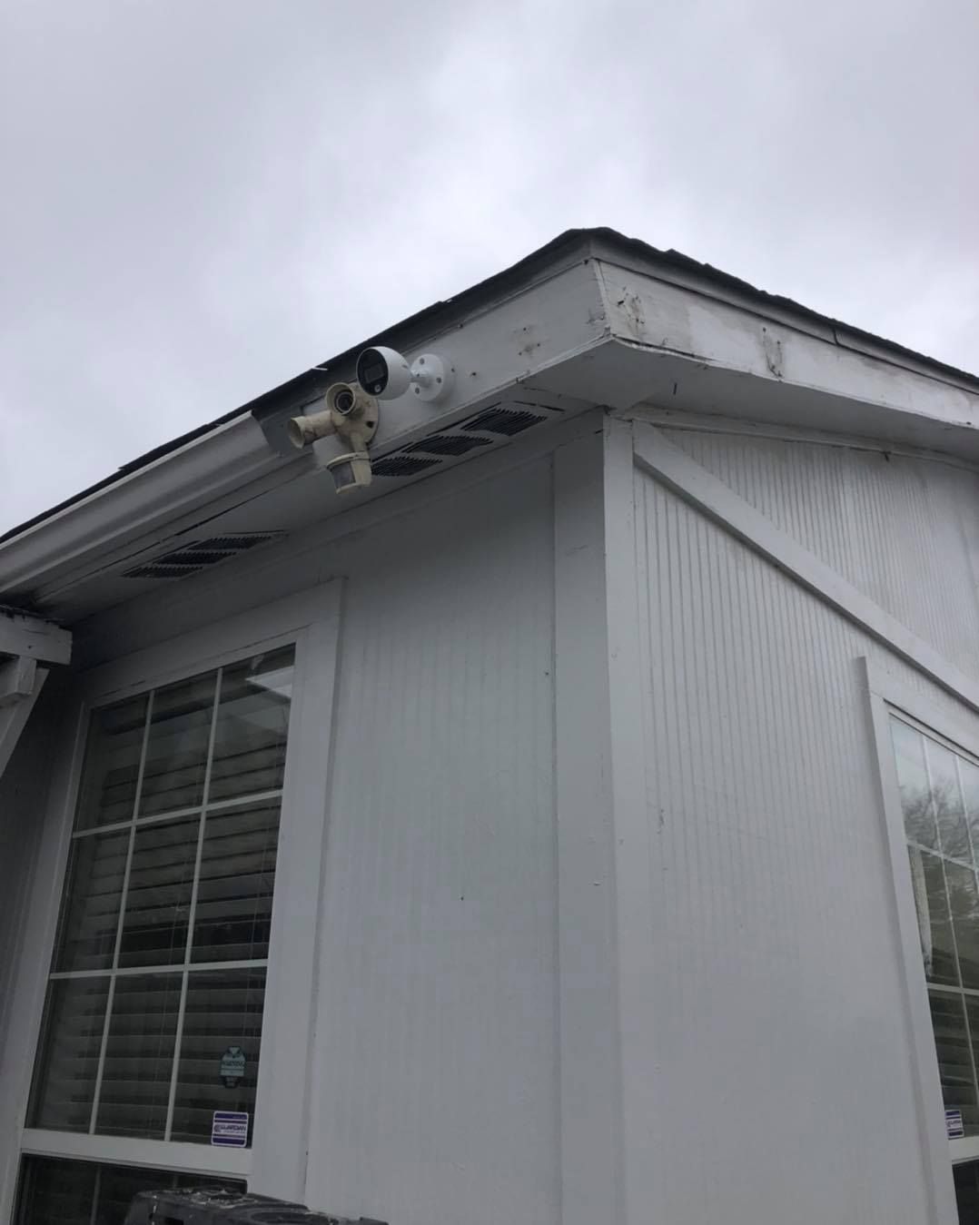 White building corner with security cameras mounted under the eaves; cloudy sky background.
