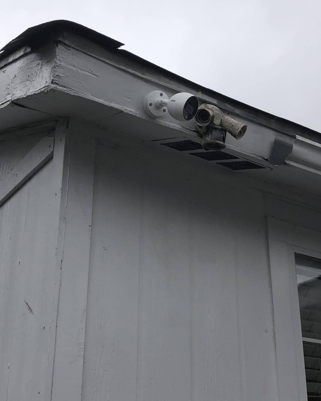 Security camera mounted on the white exterior of a building, near the roof's edge.