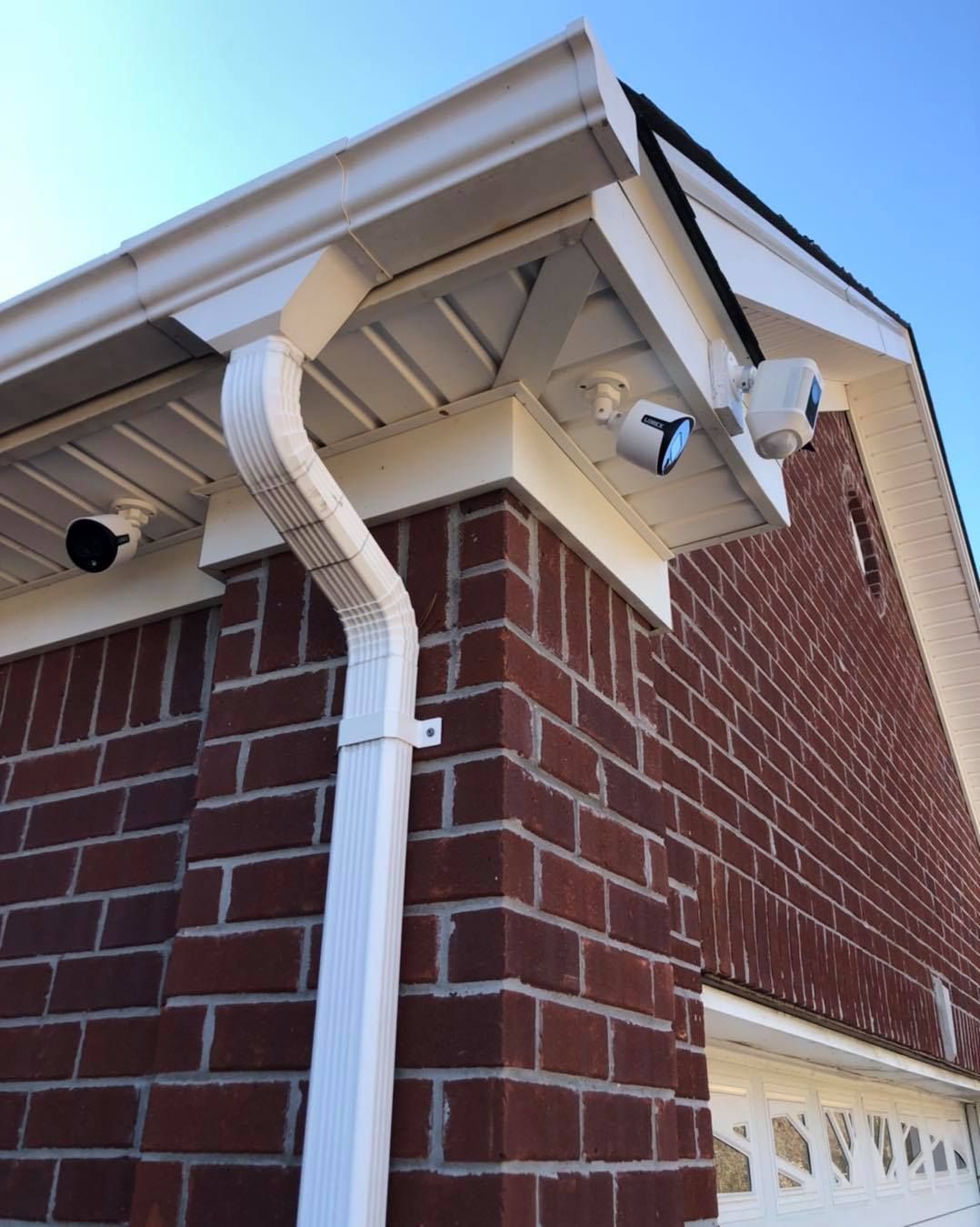 Brick building corner with white gutters, trim, and security lights; the roof is black.