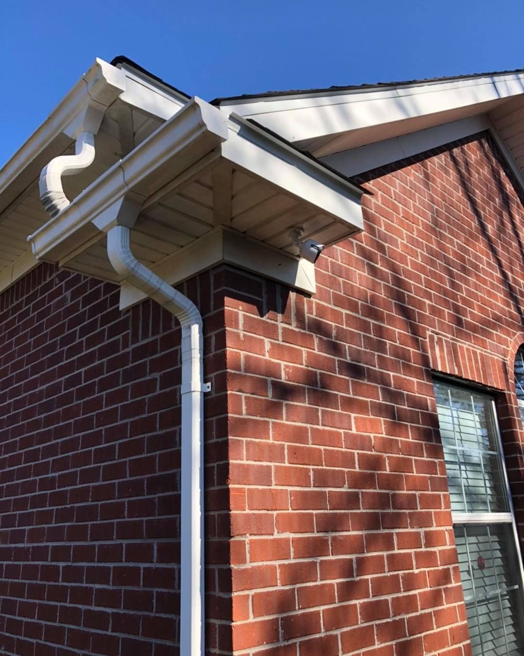White gutters and downspouts on a brick building with a blue sky background.