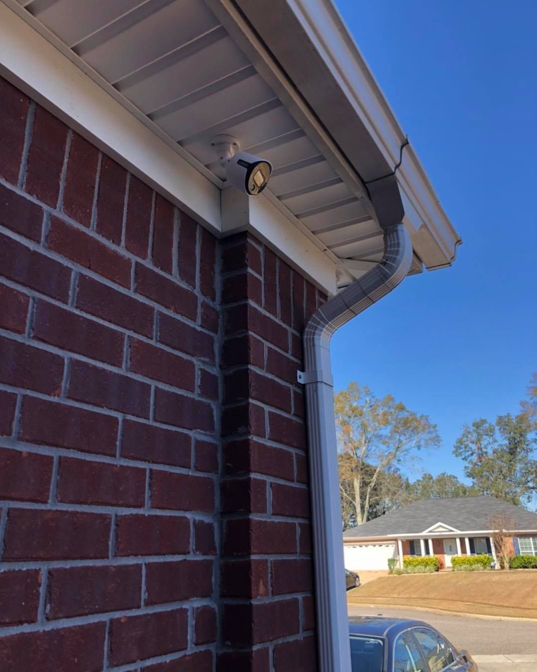 Brick house exterior with a security camera, gutter, and blue sky.