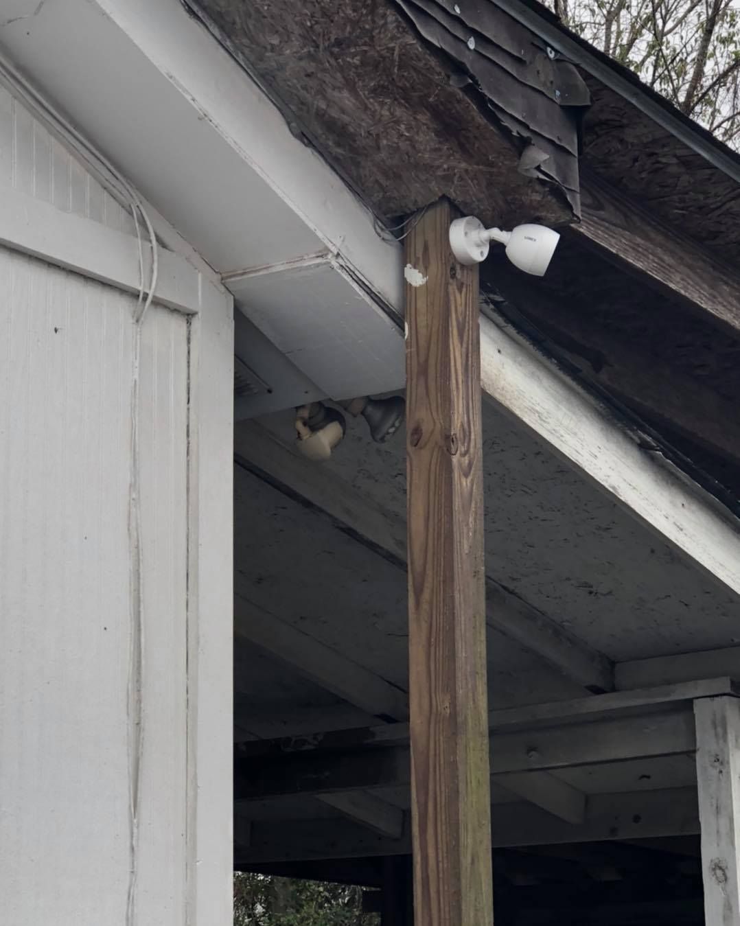 White building exterior with a security camera and a bird's nest under the roof.