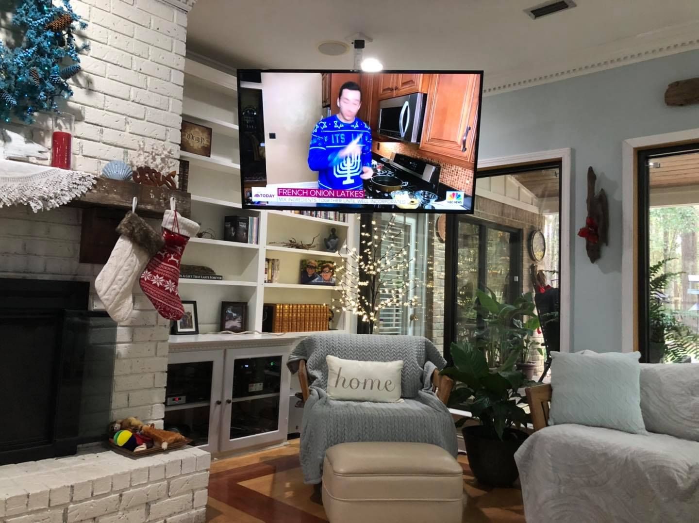 Living room with TV showing news, fireplace, bookshelf, chair, and sofa; Christmas decorations.