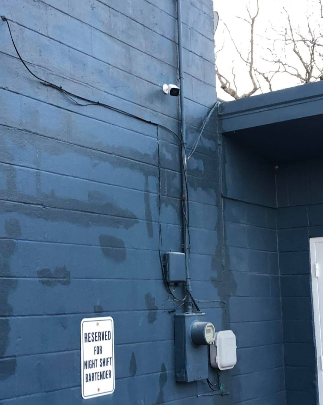 Blue building with a security camera, electrical boxes, and a sign that reads, 