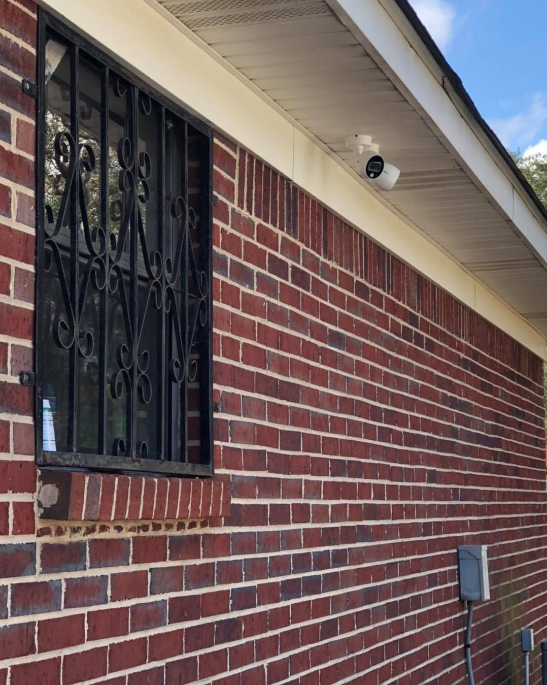 Brick building exterior with a security camera and barred window.