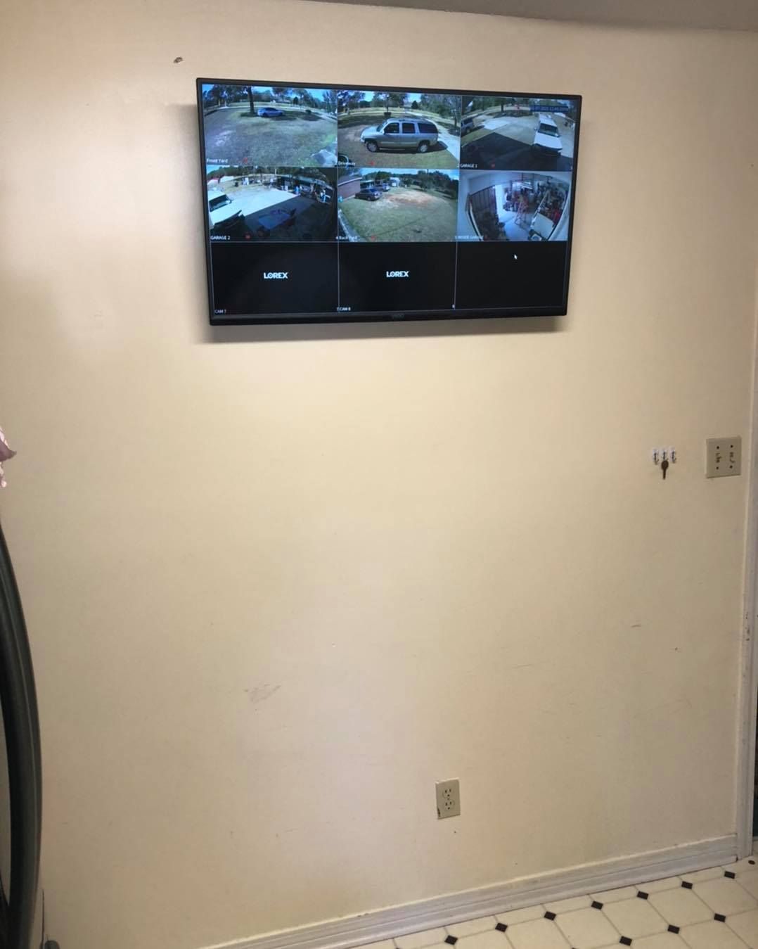 Security camera monitor on a beige wall displaying multiple camera views in a room with a tiled floor.