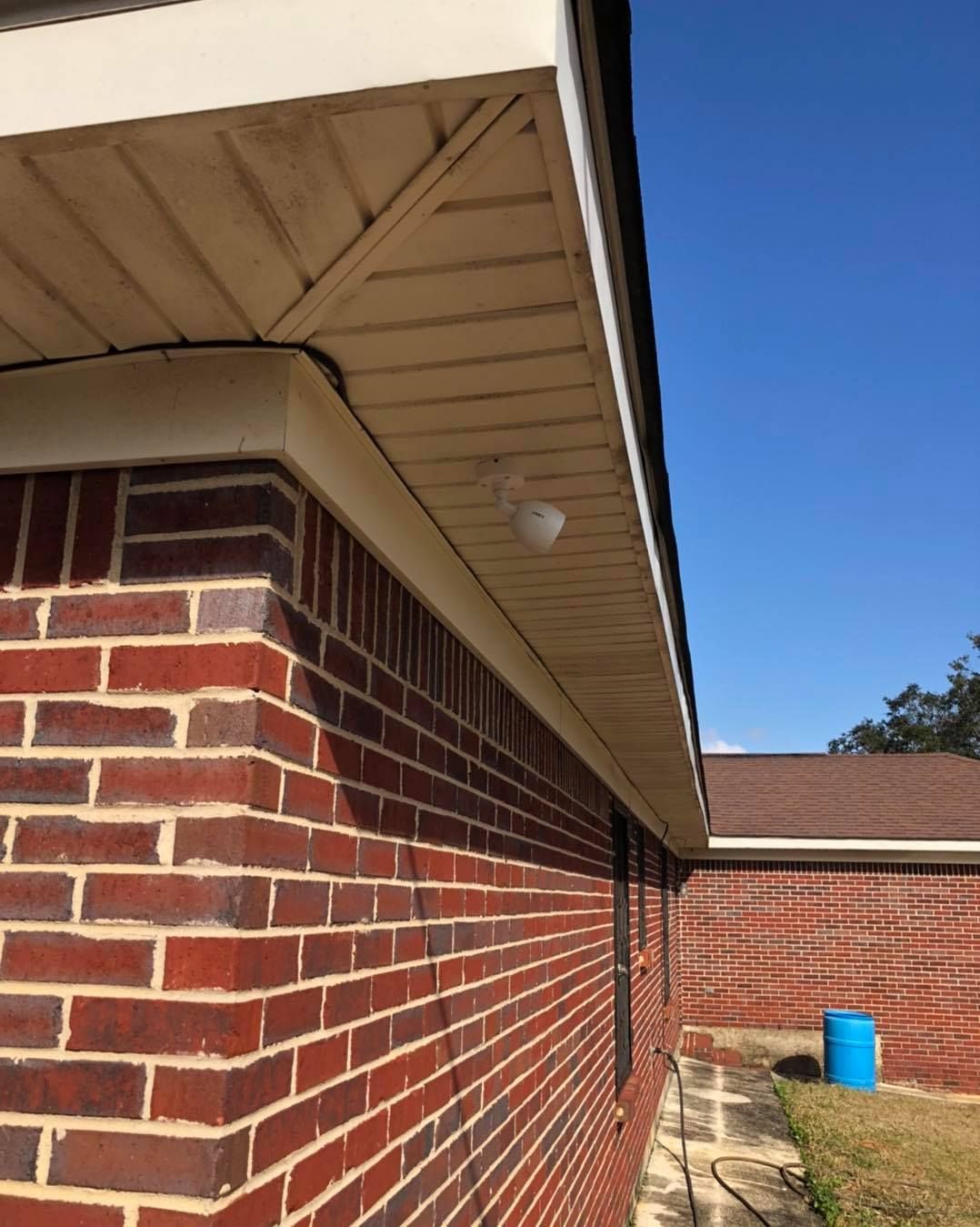 Brick building exterior with white eaves, a security camera, and blue sky.