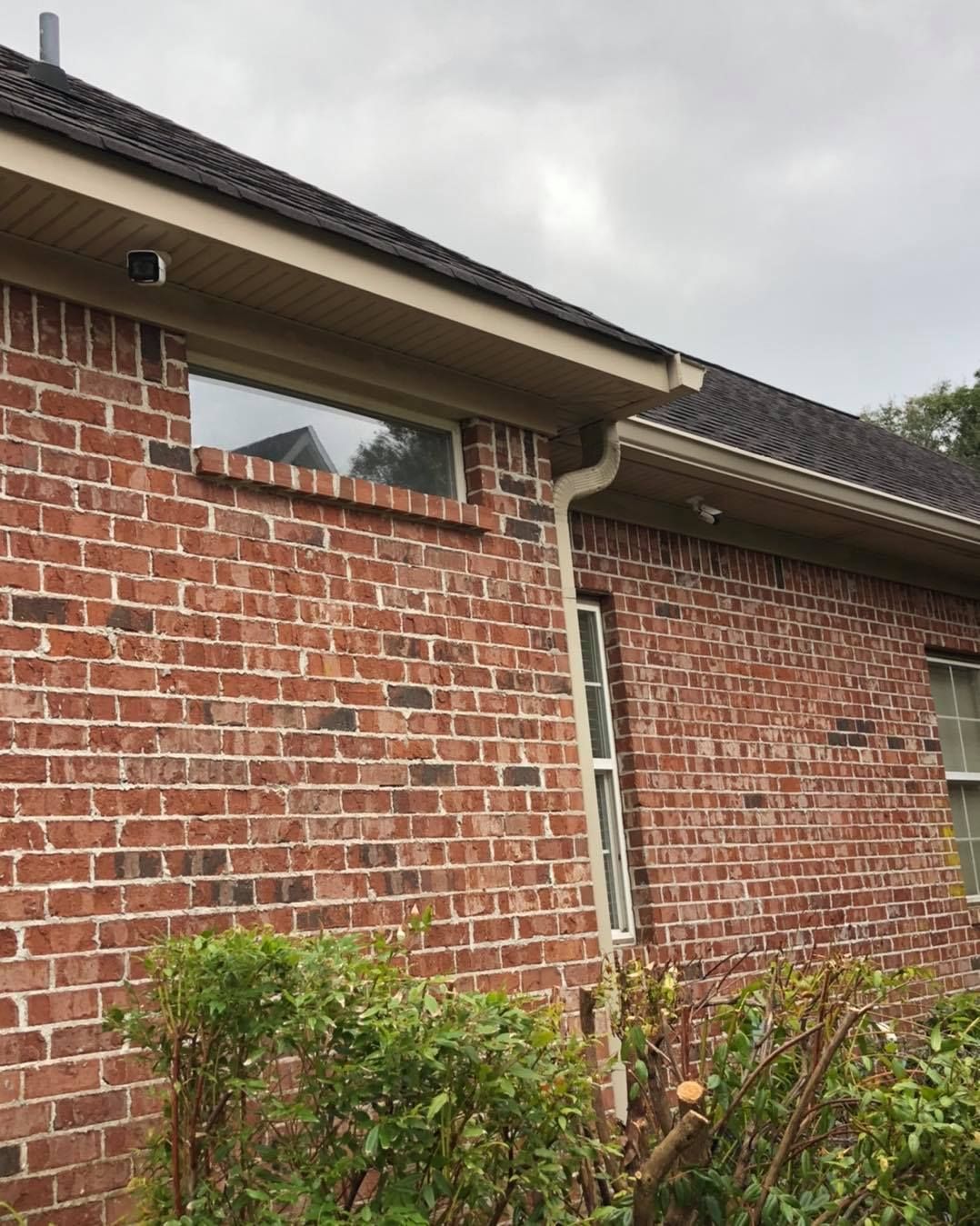 Brick building exterior with gutters, window, and bushes. Cloudy sky.