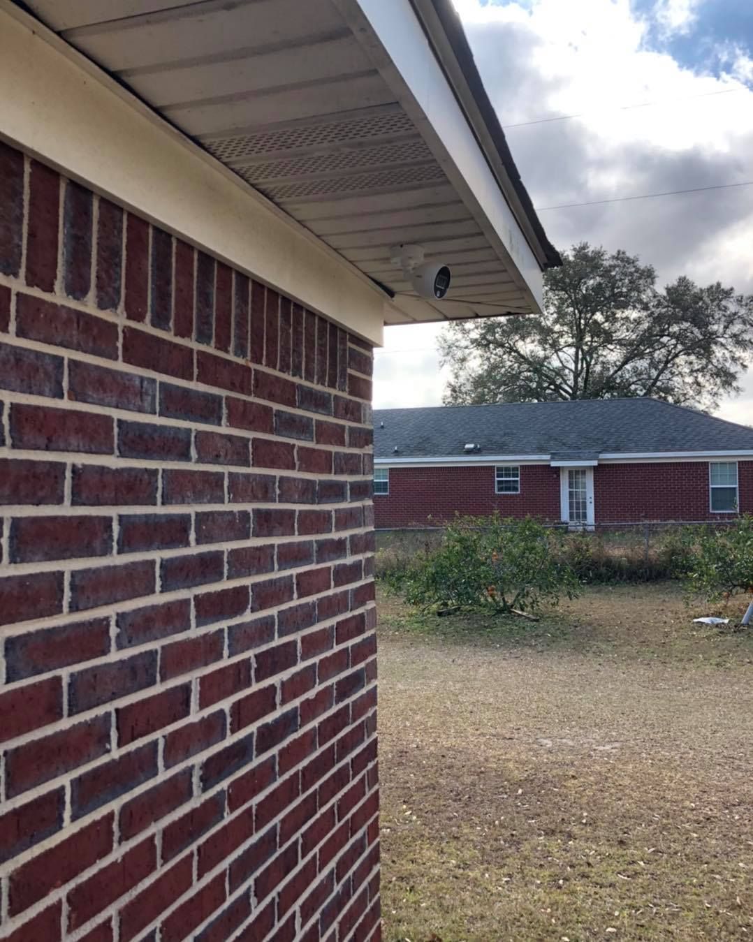 Red brick building corner with a white roof overhang, a security camera, and a view of another building.