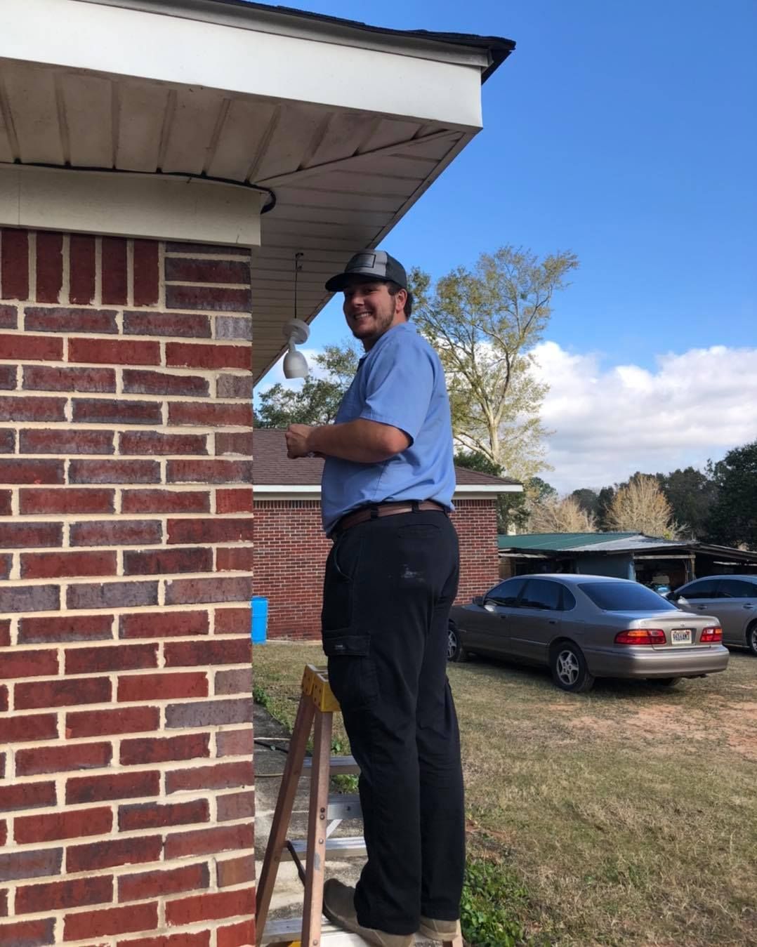 Man on a ladder, installing lights on a brick house, sunny day.