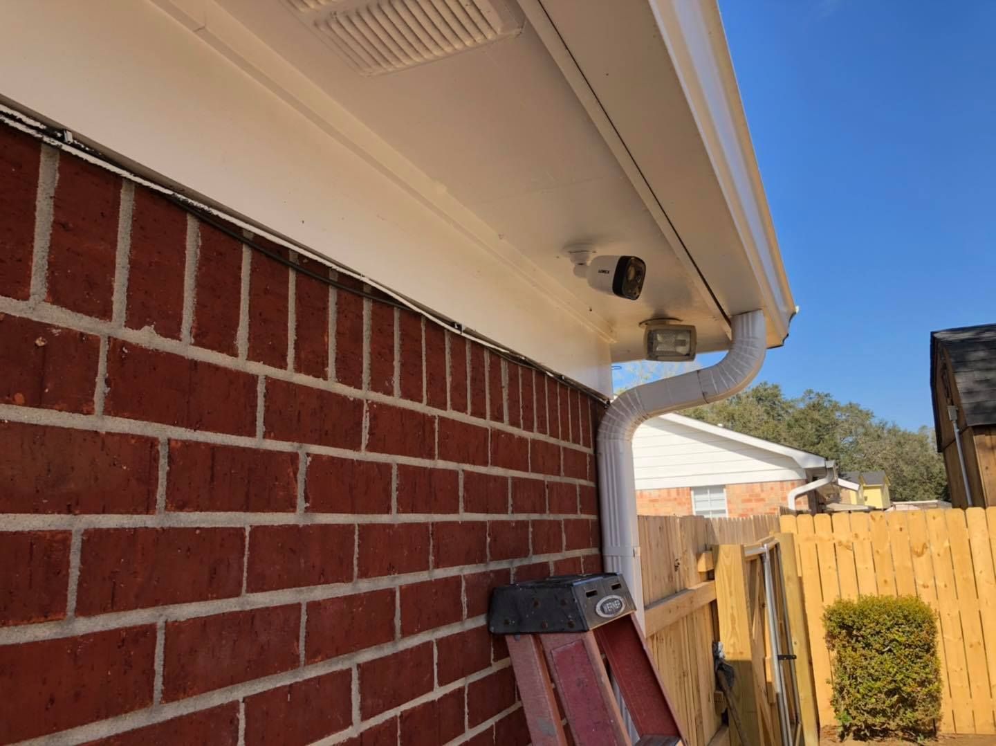 Security camera mounted under white eaves on a red brick wall, next to a white gutter.