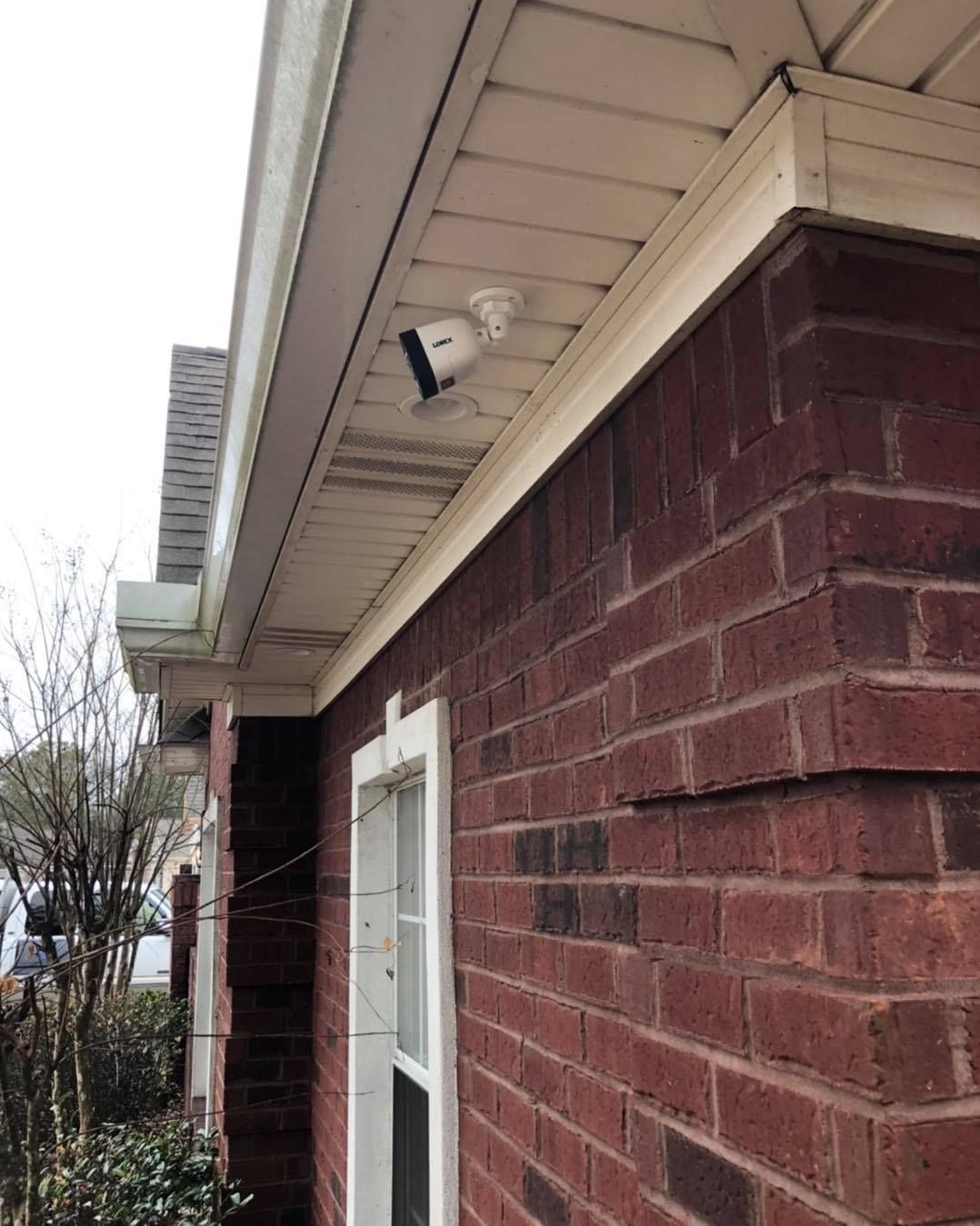 Security camera mounted under the eaves of a brick house, looking downwards.