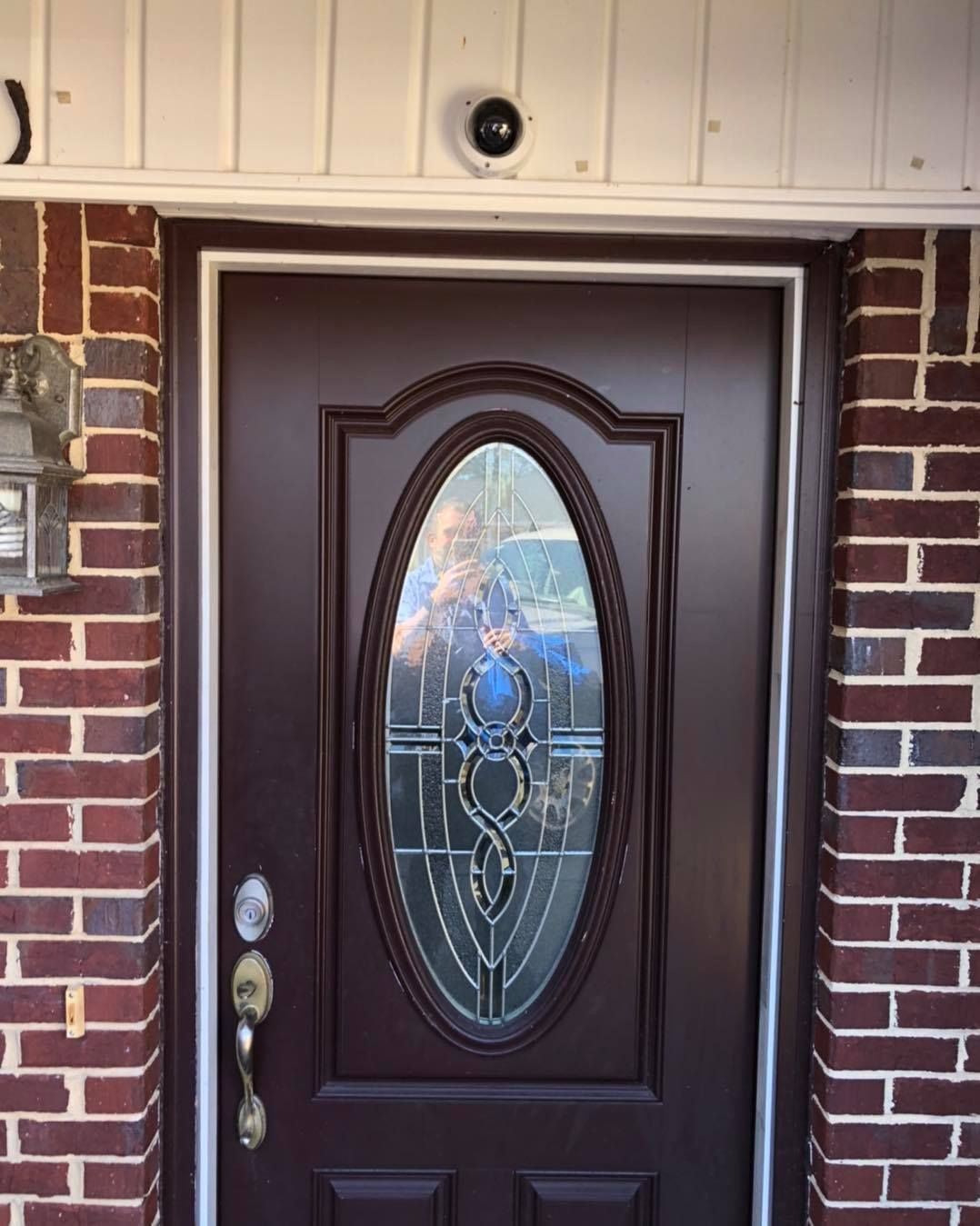Dark brown front door with oval window, flanked by brick. A security camera is above the door.