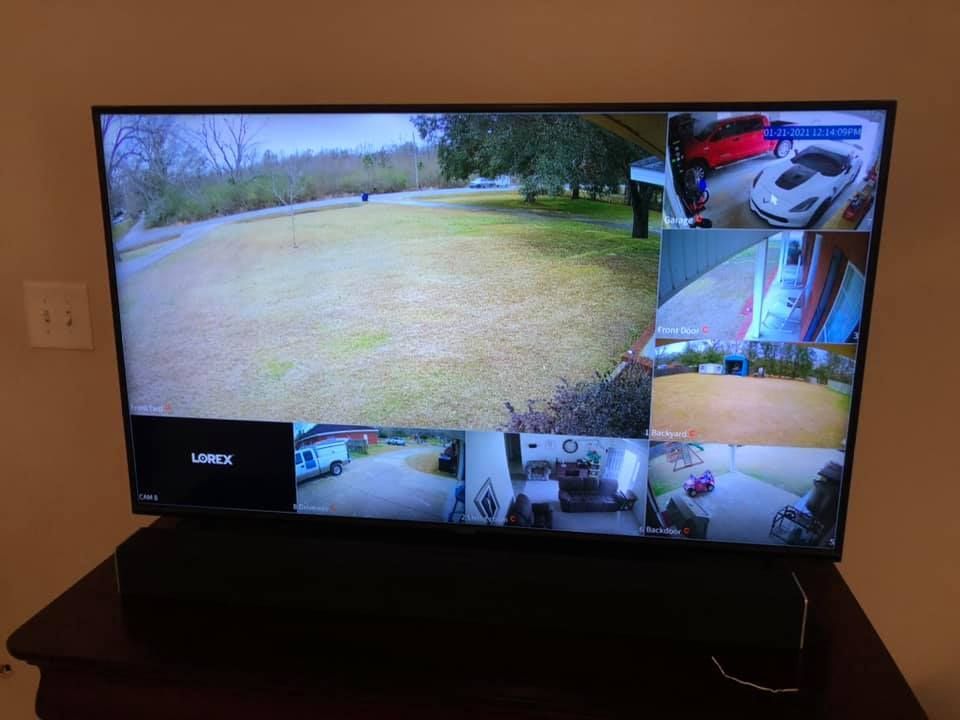 A television displaying live feeds from multiple security cameras showing a lawn, vehicles, and various indoor views.