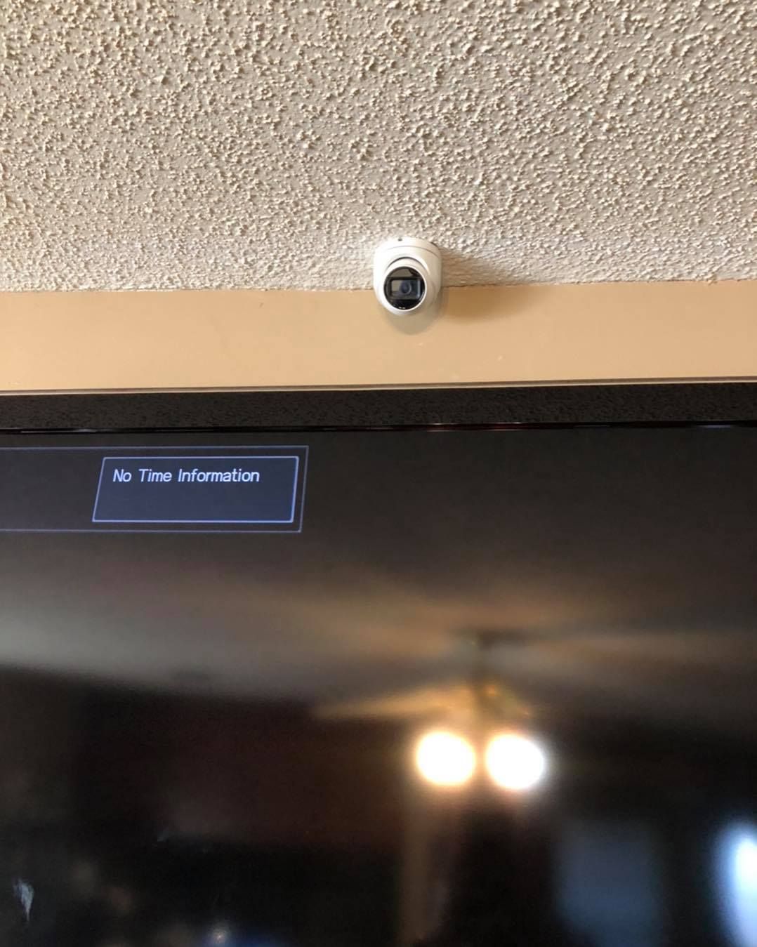A white security camera mounted on a ceiling, above a television.