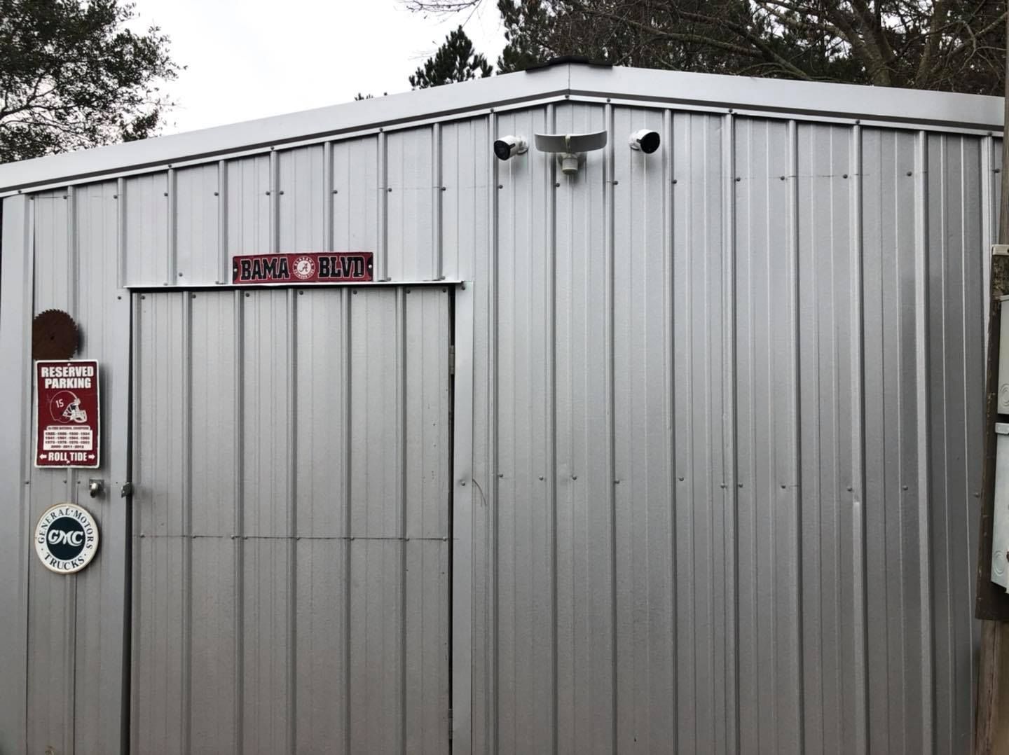 Metal shed with door, two security cameras, and signs.
