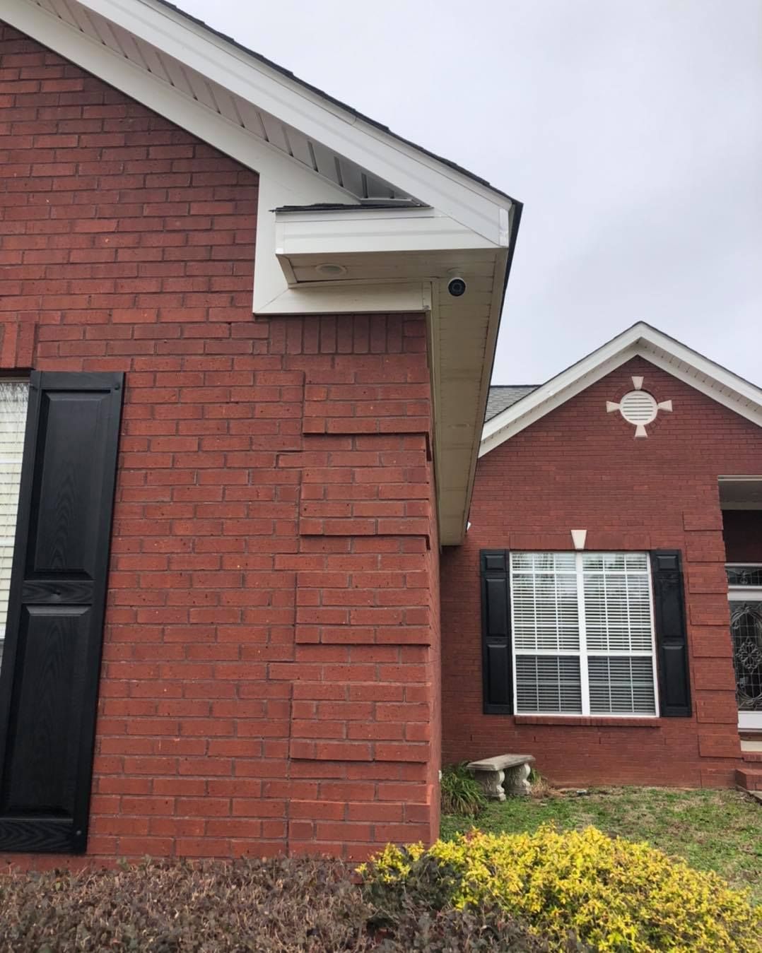 Red brick house exterior with black shutters, security camera under white eave.