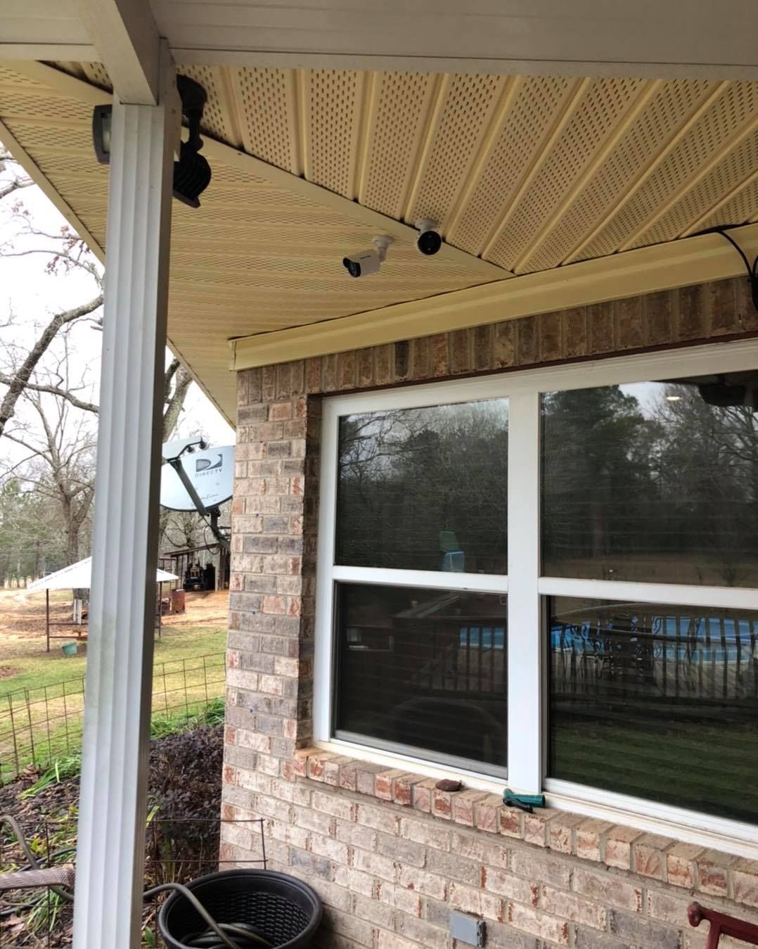 Brick house exterior with security cameras under the eaves, window overlooking a yard with a pool.