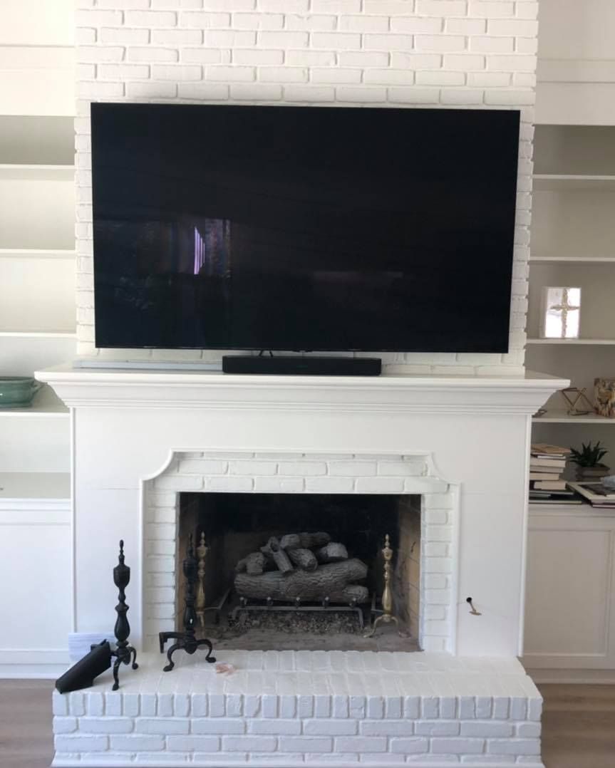 White brick fireplace with a large black TV mounted above it. Built-in bookshelves are on either side.