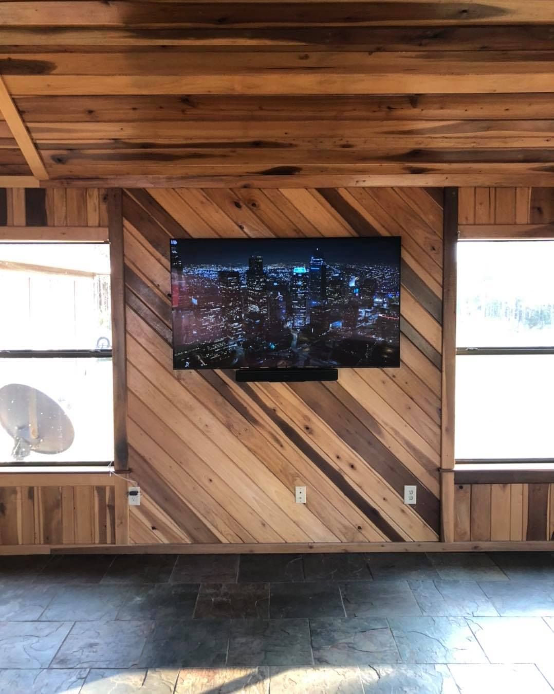 Wooden-paneled room with a TV displaying a city at night, between two windows. Ceiling and walls are also wood.