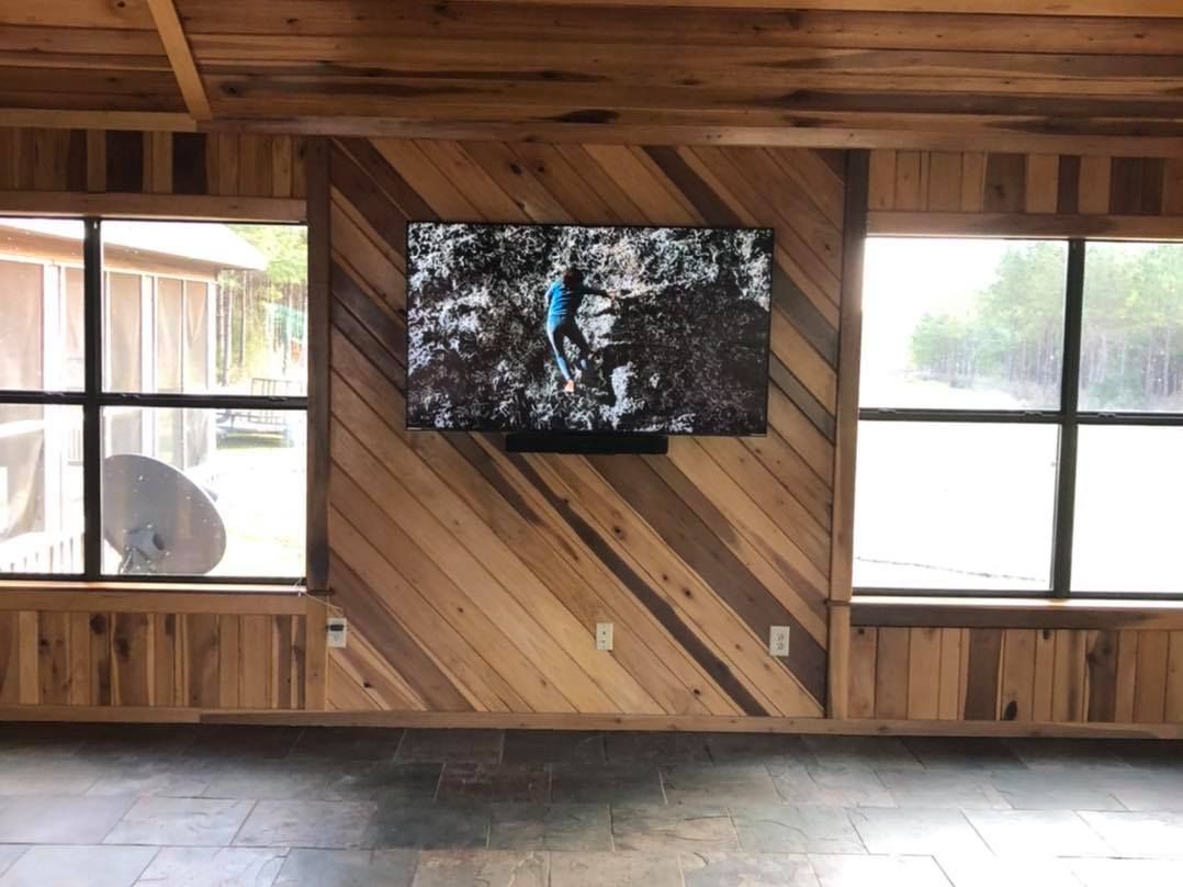 Wooden paneled room with a mounted TV between two windows.