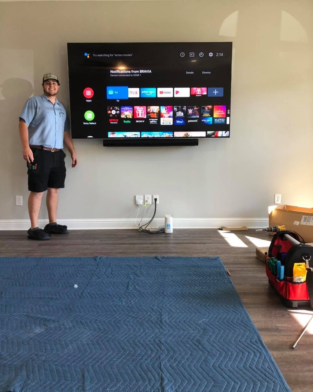 Man stands before a wall-mounted TV with soundbar, tools nearby.