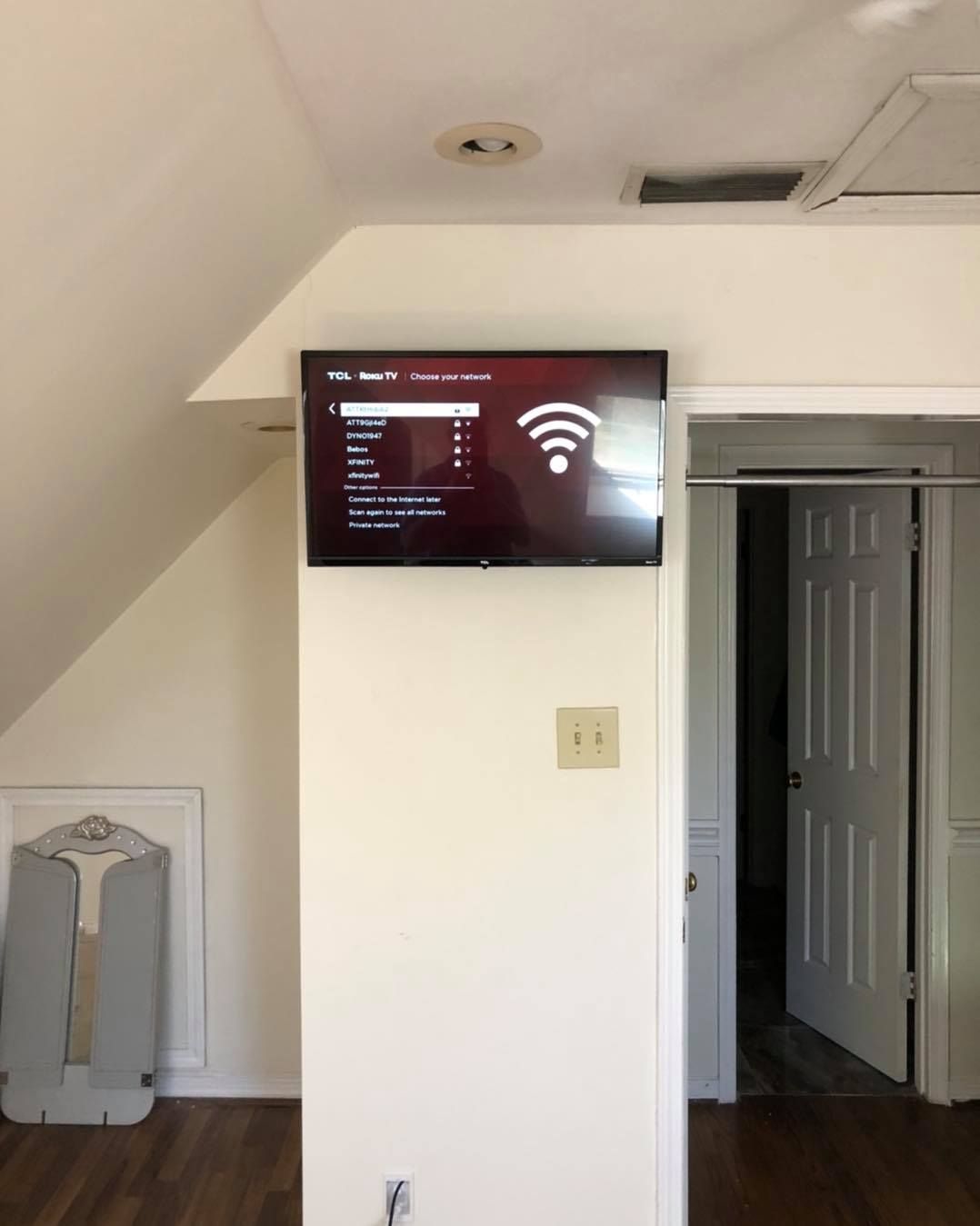 TV mounted on a white wall, displaying a Wi-Fi setup screen. Closet and slanted ceiling visible.