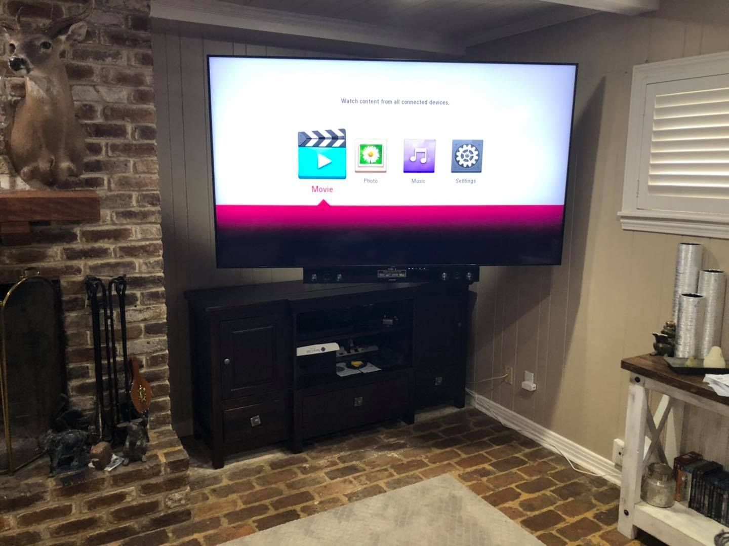 Large TV mounted above a black cabinet, against a brick wall in a living room.