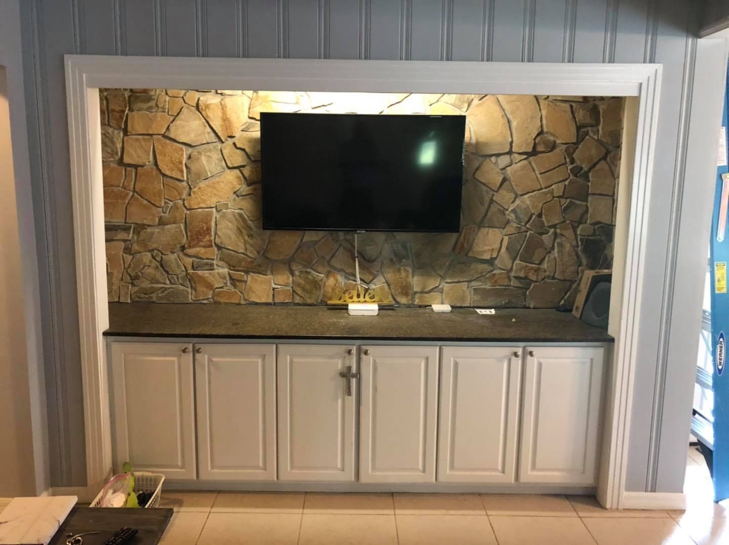 White cabinets with a TV mounted on a stone wall inside a recessed alcove.