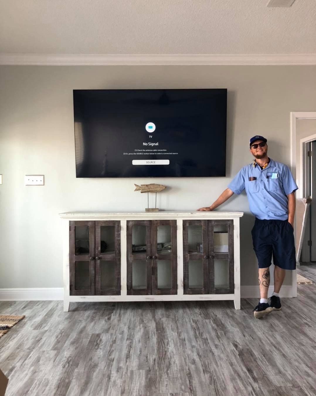 Man standing by a wooden TV stand and mounted TV in a living room.