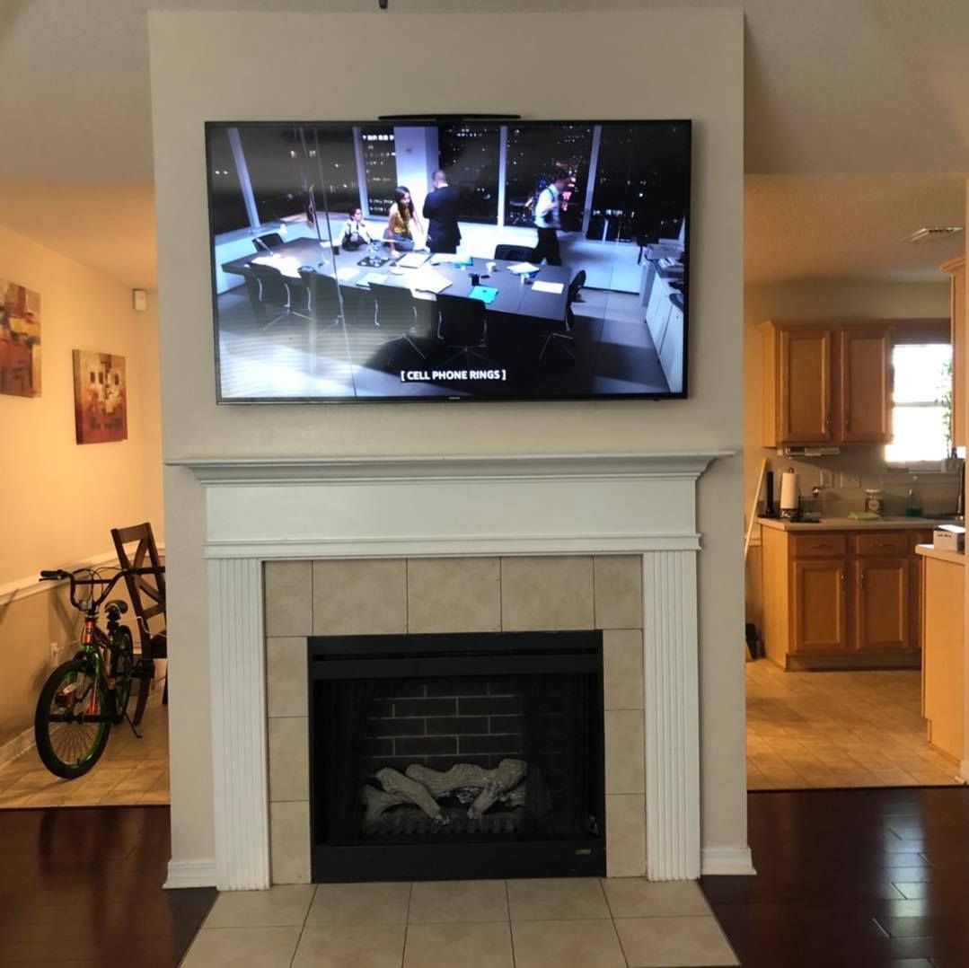 Living room with TV above fireplace, kitchen to the right, and bicycle to the left.